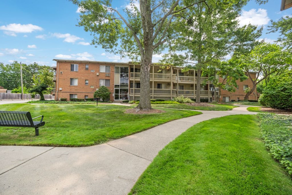 a building with a green lawn and trees and a sidewalk