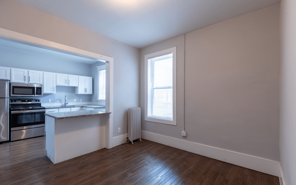 an empty living room with a window and a kitchen