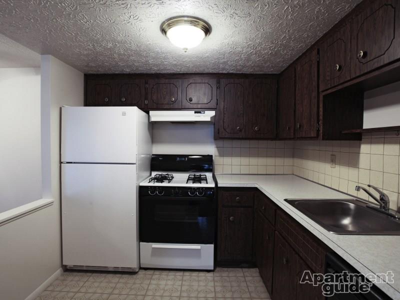Dark kitchen cabinetry with beige tile flooring, beige tile backsplash, and white appliances with black accents.