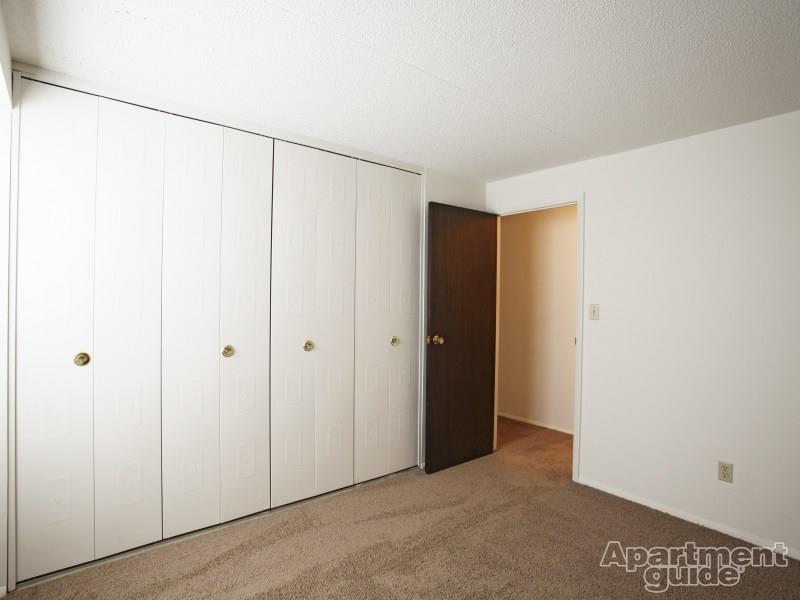 Bedroom with beige carpeting and white closet doors lining the entire right wall.