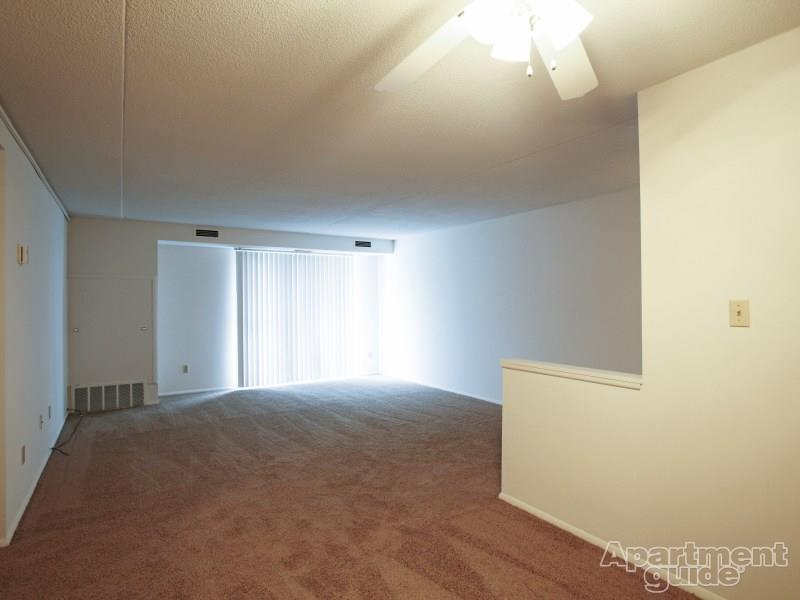 Living room with beige carpeting, vertical blinds on doorwall, and ceiling fan