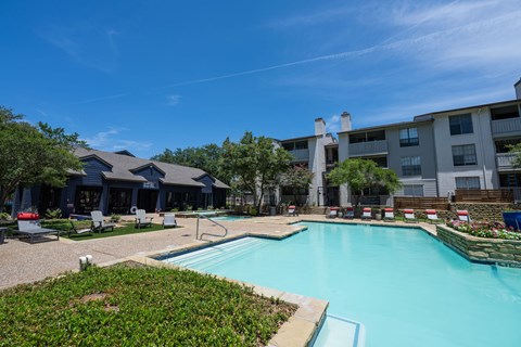 A large swimming pool surrounded by a grassy area and a building in the background.
