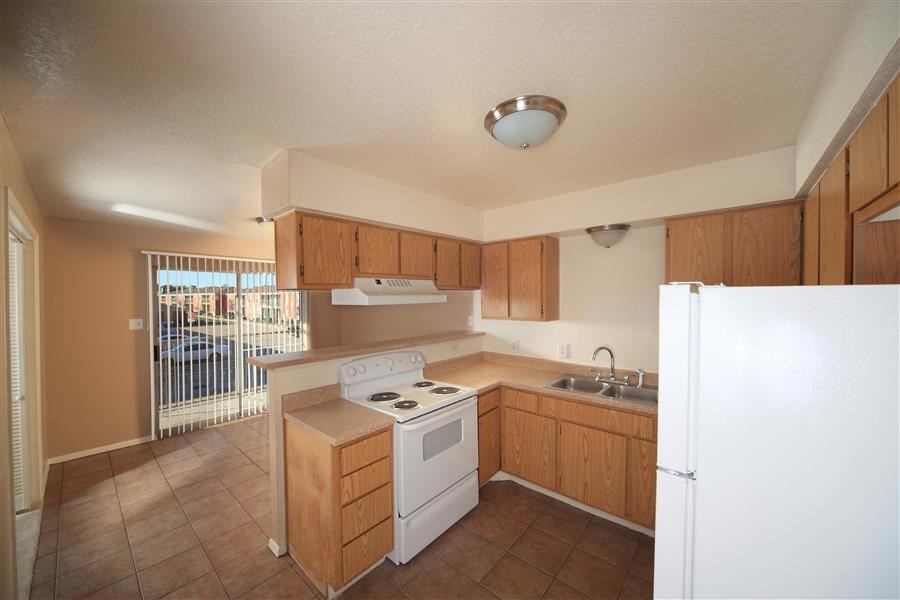 Kitchen with white appliances, stainless steal sink, brown cabinets, and tile like floor. The kitchen is open to the dinning room that opens to the patio with sliding glass doors.
