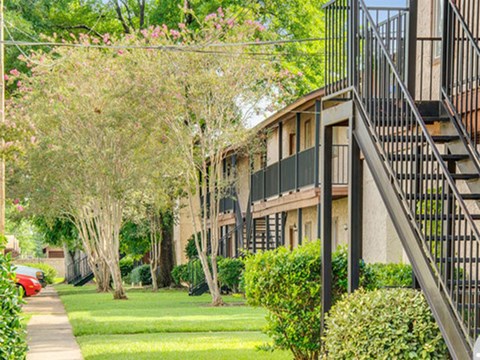 a row of apartment buildings with a lawn and trees