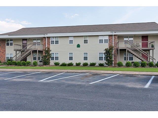 Exterior image of Hallmark Gardens. Shows asphalt parking lot in front of buildings with yellow siding and red brick, stairs leading to second level with red doors.