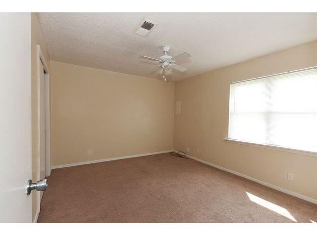 Bedroom with beige walls and beige carpet. White ceiling fan and a large window on the right wall with white horizontal blinds, closet on left wall with closed doors.