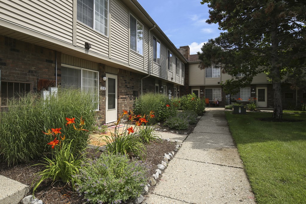 a sidewalk in front of an apartment building with flowers at Village Club of Rochester Hills, Shelby Township, MI 48317