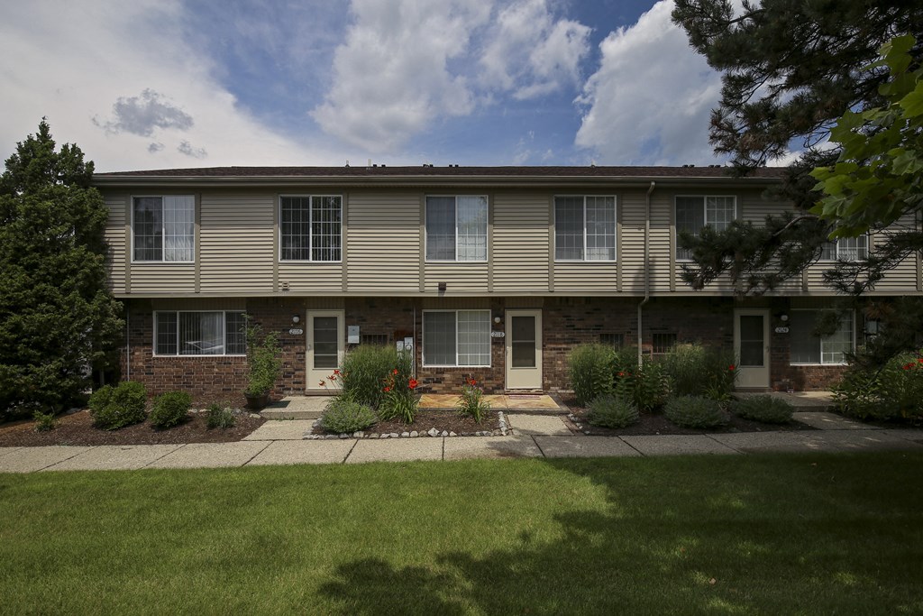 an apartment building with a lawn and plants in front of it at Village Club of Rochester Hills, Shelby Township