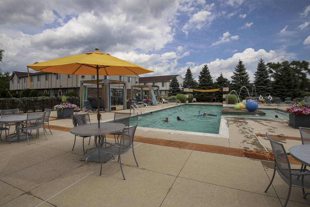 a swimming pool with tables and umbrellas and people in it at Village Club of Rochester Hills, Shelby Township, MI 48317