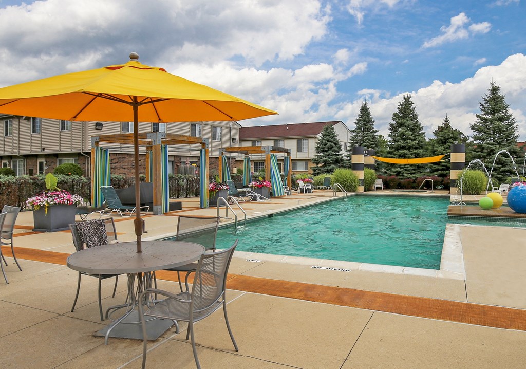 our apartments have a swimming pool and patio with chairs and umbrellas at Village Club of Rochester Hills, Shelby Township, MI