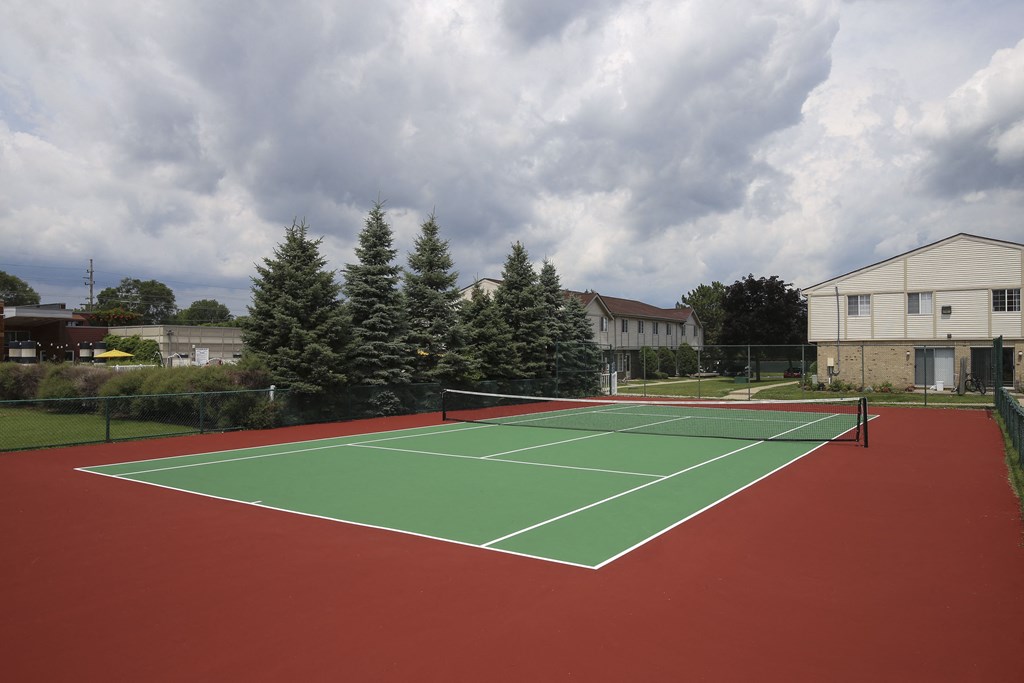 a tennis court with a house and trees in the background at Village Club of Rochester Hills, Michigan