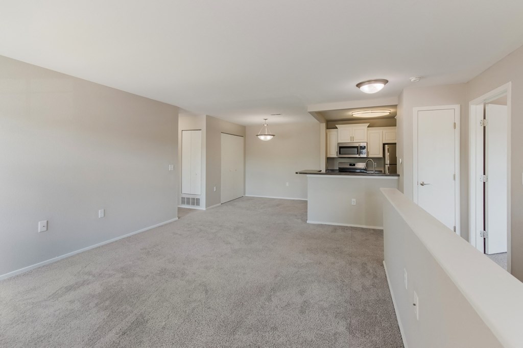 an empty living room and kitchen with white walls and carpet