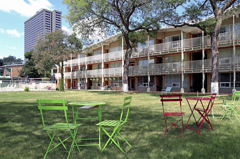 a row of colorful chairs and tables in a grassy area in front of an apartment building