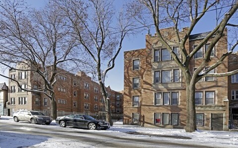 A row of brown buildings with cars parked in front.