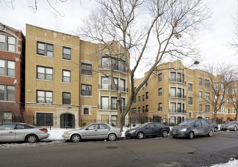 A row of apartment buildings with cars parked in front.