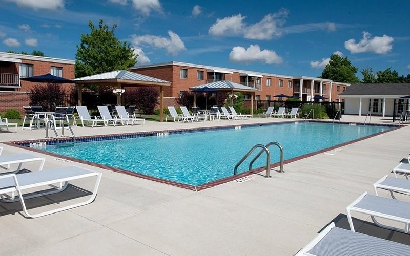 A swimming pool surrounded by sun loungers and apartment buildings.