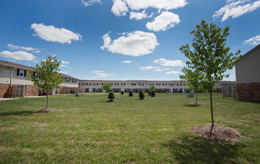 A grassy field with trees and a building in the background.