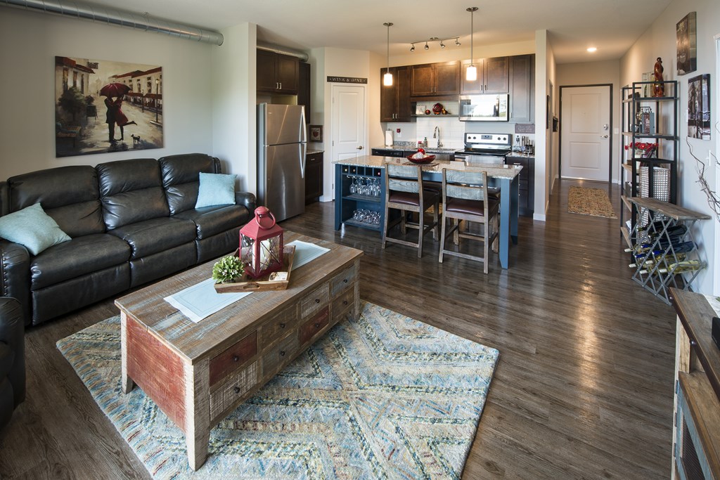 A living room with a black couch and a coffee table with a red vase on it.