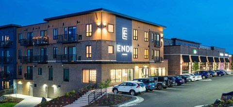 The image shows a building with the word "END" on it, with cars parked in front and a clear sky in the background.
