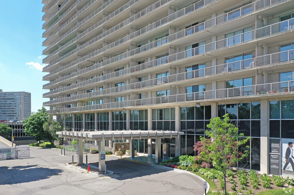 Exterior of the Jefferson. The image shows the parking lot and main enterance to the building. The building stands 30 stories tall. There is green flowers around the outside of the building.