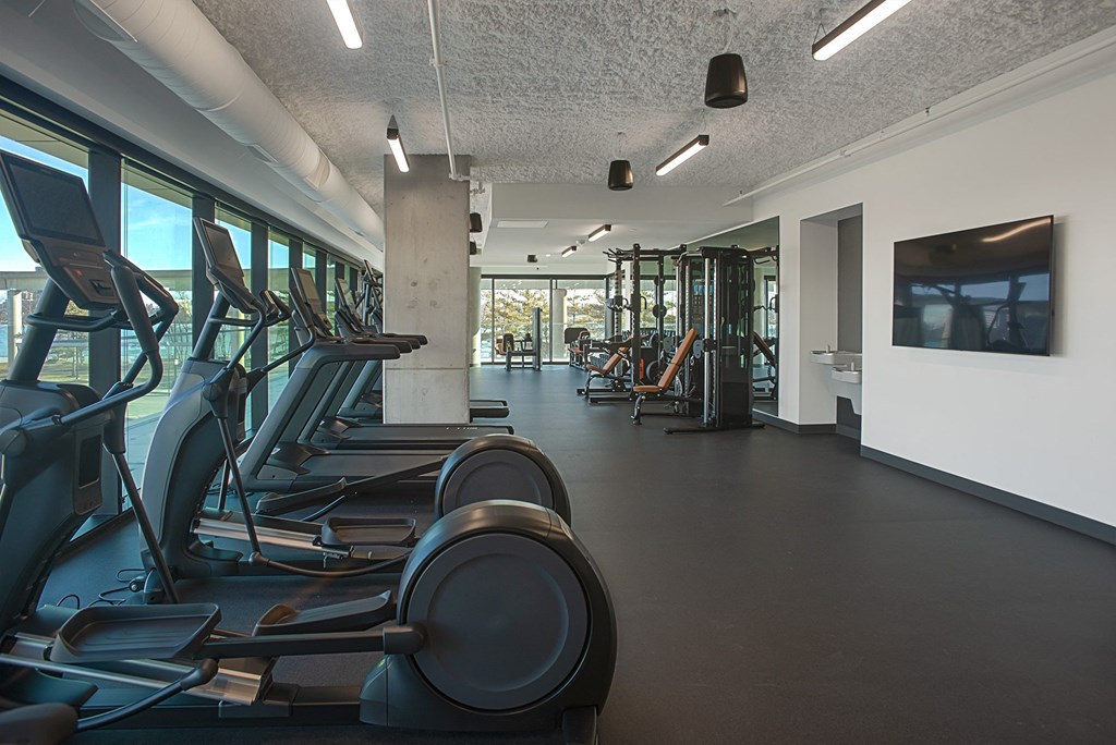 a gym with cardio equipment and a tv