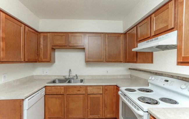 Kitchen with white appliances, brown cabinets, tan counters, and tile-like flooring. - Photo Gallery 2
