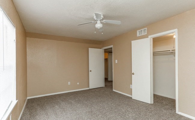 Bedroom with brown walls, brown plush carpeting, spacious closets, and a white ceiling fan. - Photo Gallery 5