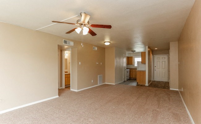 Living room with brown plush carpeting, brown walls, and a ceiling fan. The floor plan is open to the kitchen and entry. - Photo Gallery 3