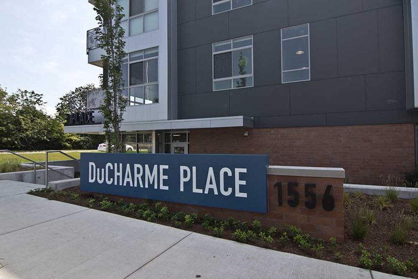 Exterior image of DuCharme Place's monument sign. Grey building is in background.