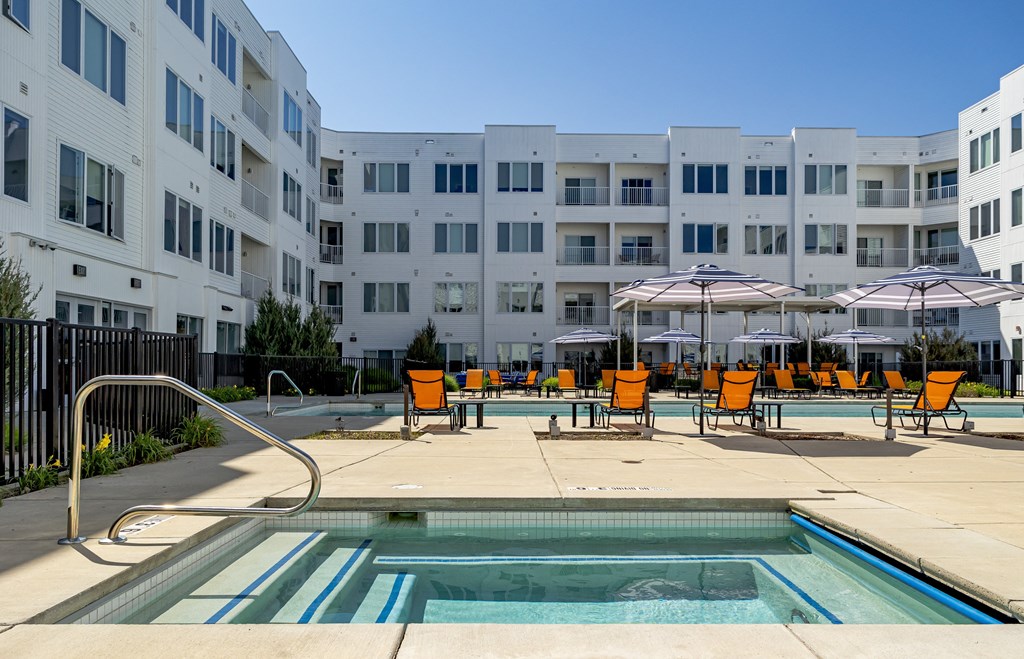 a pool with yellow chairs and umbrellas in front of an apartment building