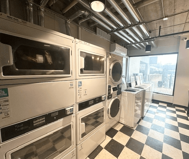 A row of stainless steel ovens are lined up in a room with a checkered floor at City Club Apartments Lafayette Park, Detroit