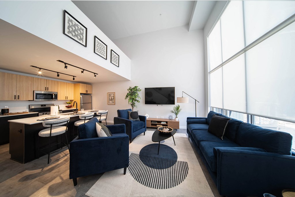 a living room with blue couches and chairs and a kitchen with a large window