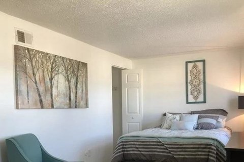 A bedroom with a bed, chair, and two pictures on the wall.