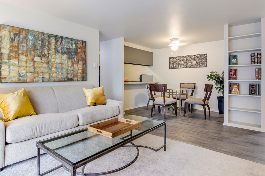 A living room with a white couch, a glass coffee table, and a painting on the wall.
