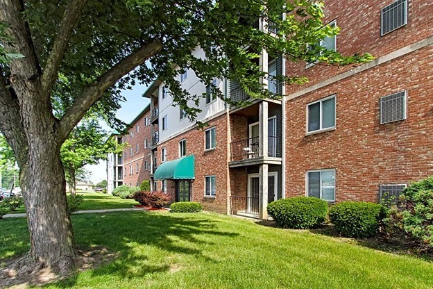 a grassy area with a tree in front of a brick building