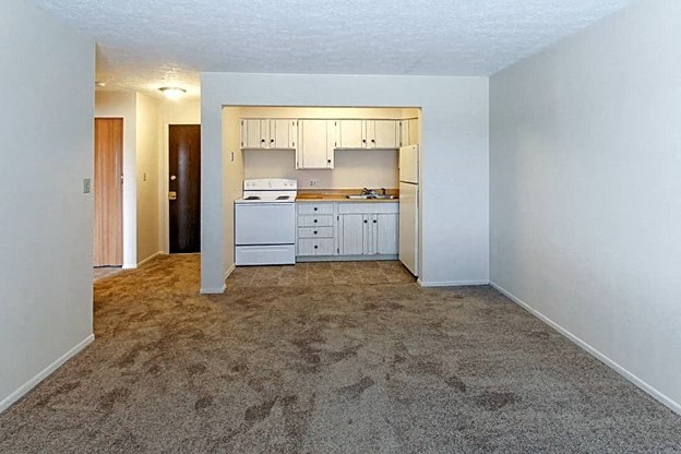 an empty living room with a kitchen in the background