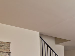 Living Area With Stairs To Upper Level Living room with two yellow chairs on right wall and artwork of plant above, pink/orange couch on left wall and coffee table in center of room. Stairs to upper level in background.
