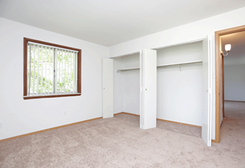 Bedroom with white walls, tan carpeting, a large window, and two large closets. - Photo Gallery 5