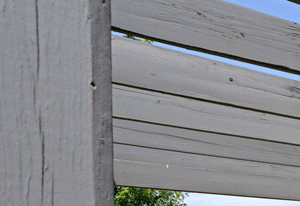 BBQ grill and green picnic table on cement slab under wood pergula
