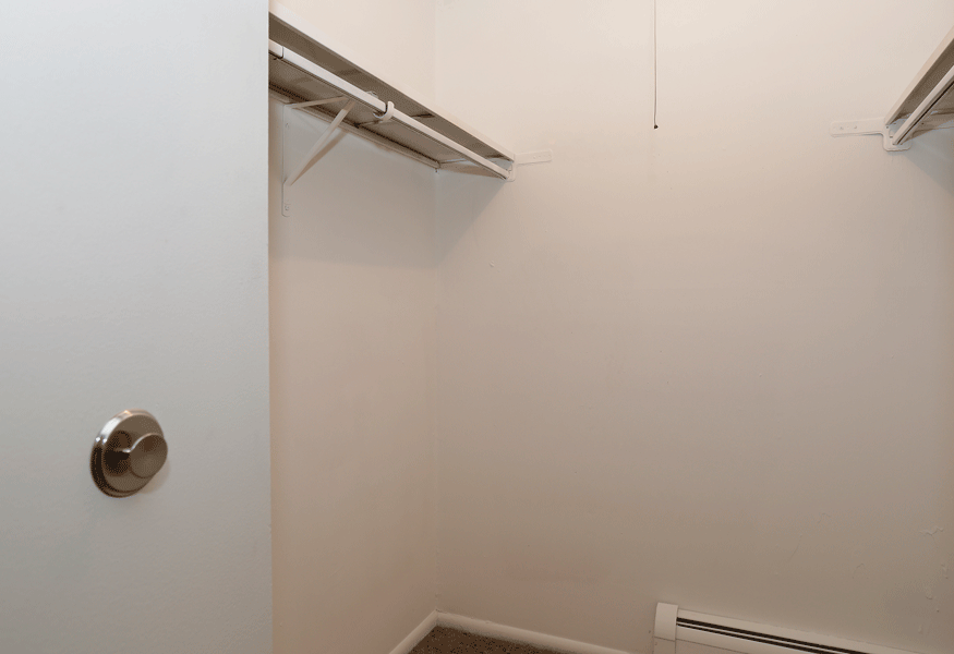 a walk in closet in a white room with a white wall and a silver door