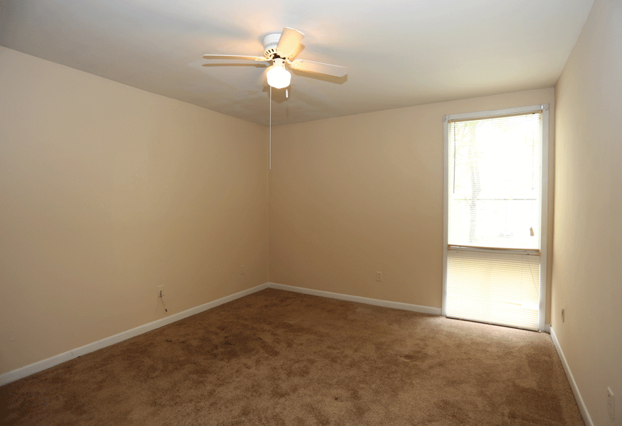 Bedroom with ceiling fan and tan carpeting and a large window.