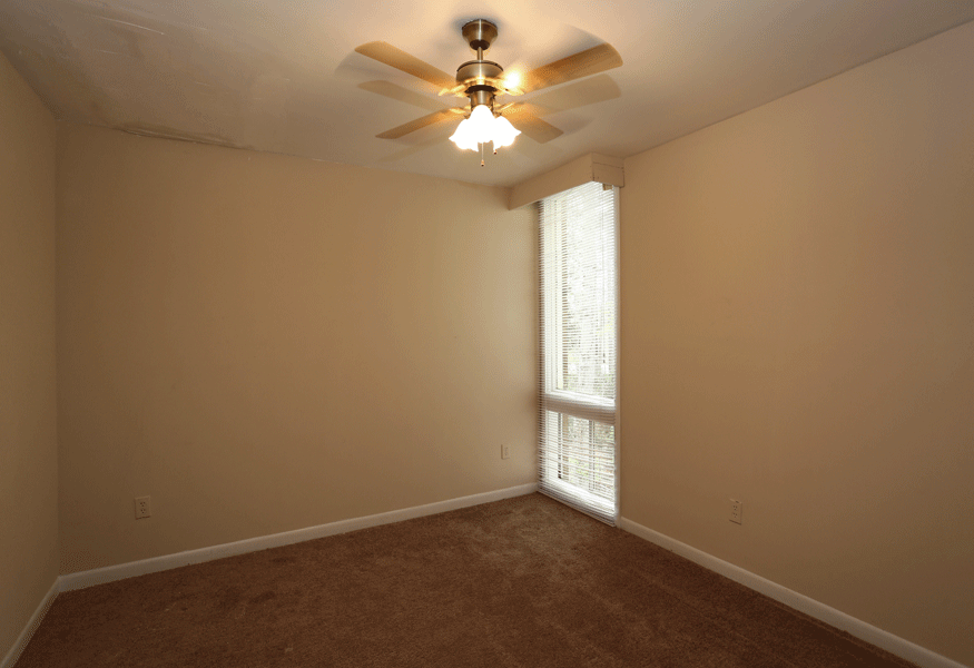 Bedroom with ceiling fan and tan carpeting and a large window.