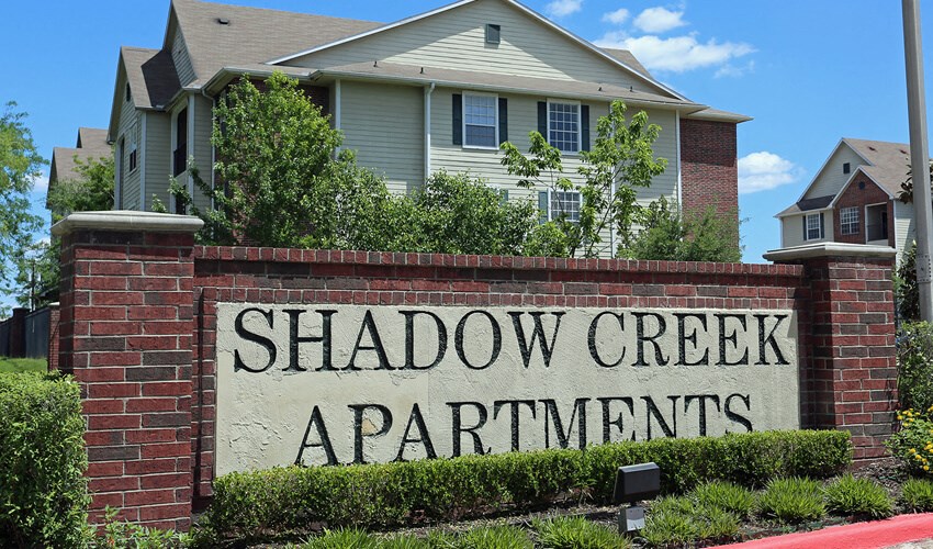 a sign for shadow creek apartments in front of a house