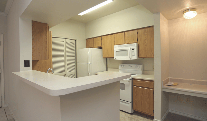 Kitchen with light wooden cabinets, white appliances, and white counters. The kitchen has a L-shaped bar.