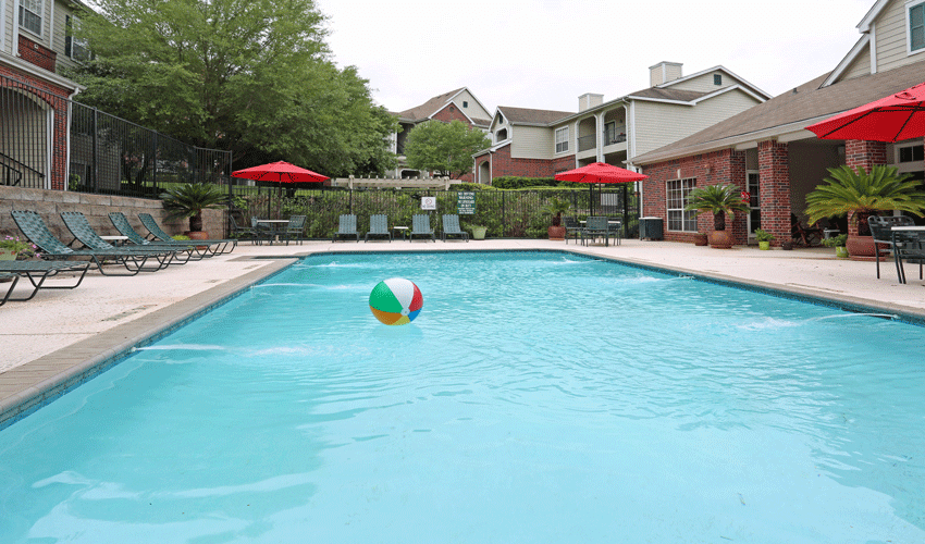 Sparking outdoor swimming pool and expansive sundeck with pool furniture.  There is a multicolored beach ball floating in the pool.