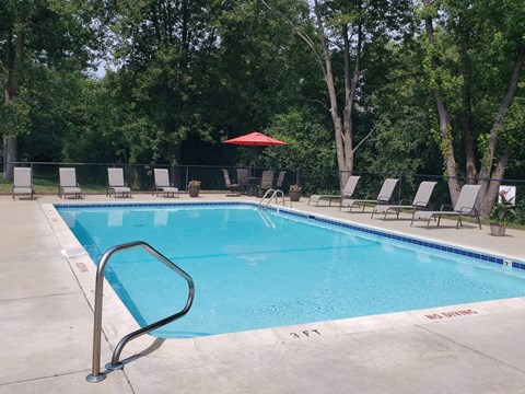 Rectangle pool with brown lawn chaairs, table with 4 chairs and red umbrella in back corner