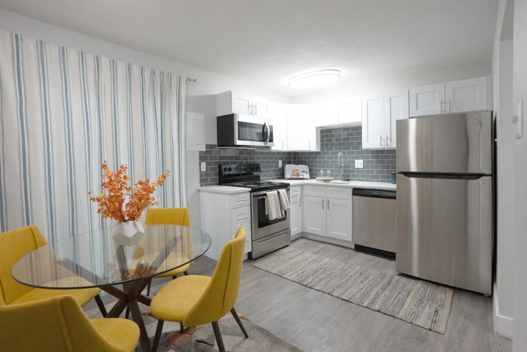 A modern kitchen with a glass table and yellow chairs.