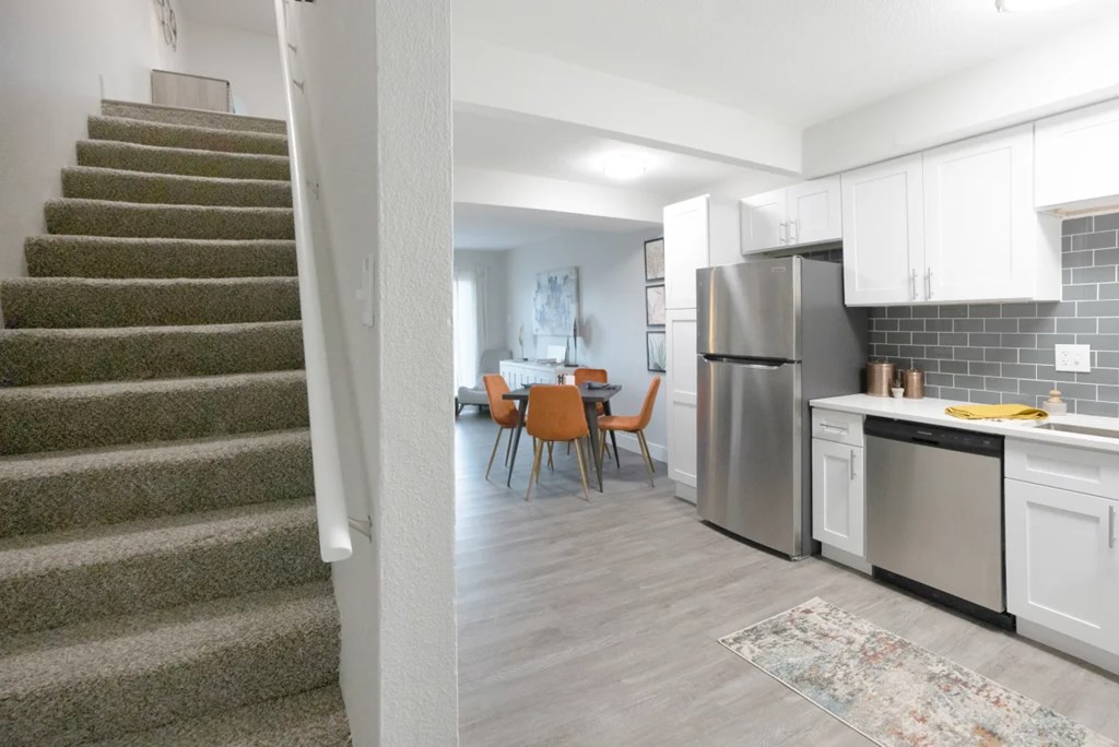 A kitchen with a refrigerator, stove, and chairs.