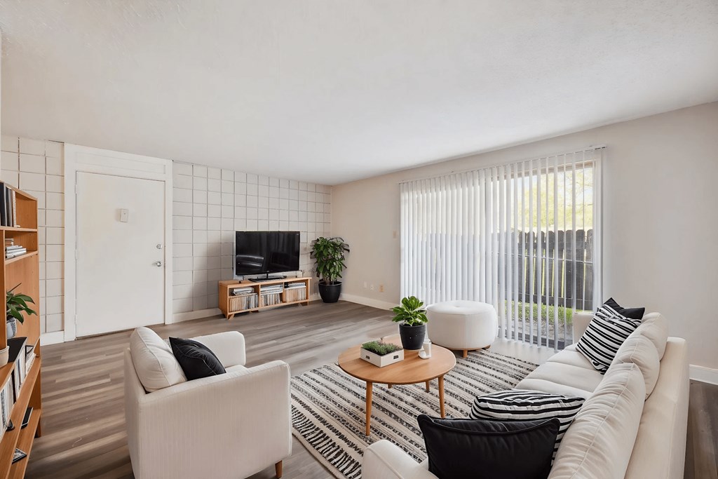 A living room with a white couch, a black and white striped pillow, a wooden coffee table, and a flat screen TV.