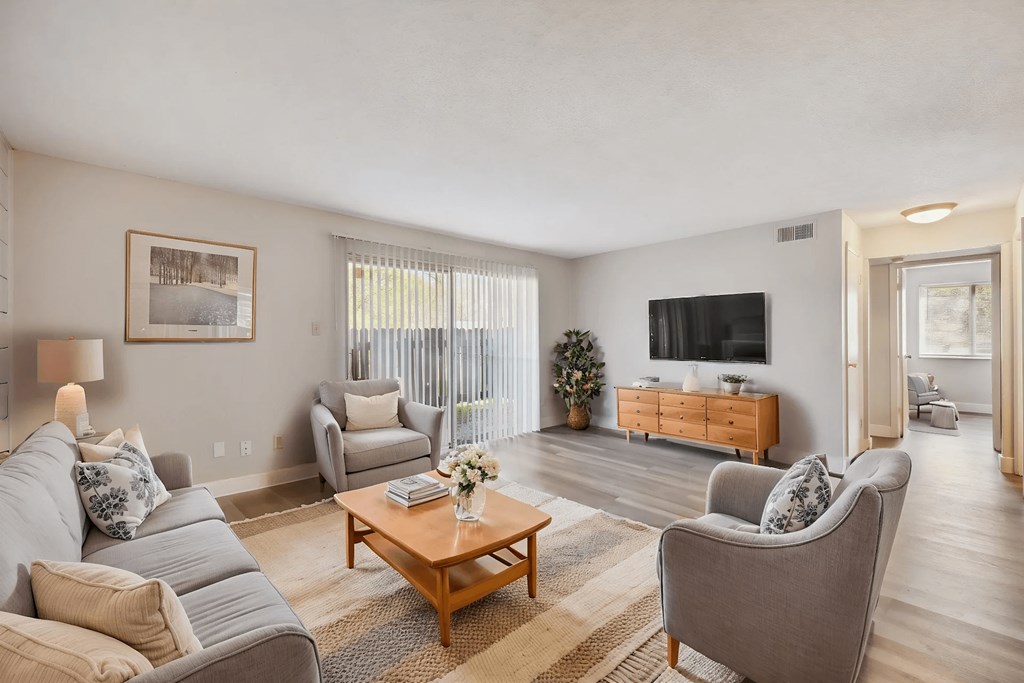 A living room with a grey couch, a wooden coffee table, and a flat screen TV on a wooden cabinet.